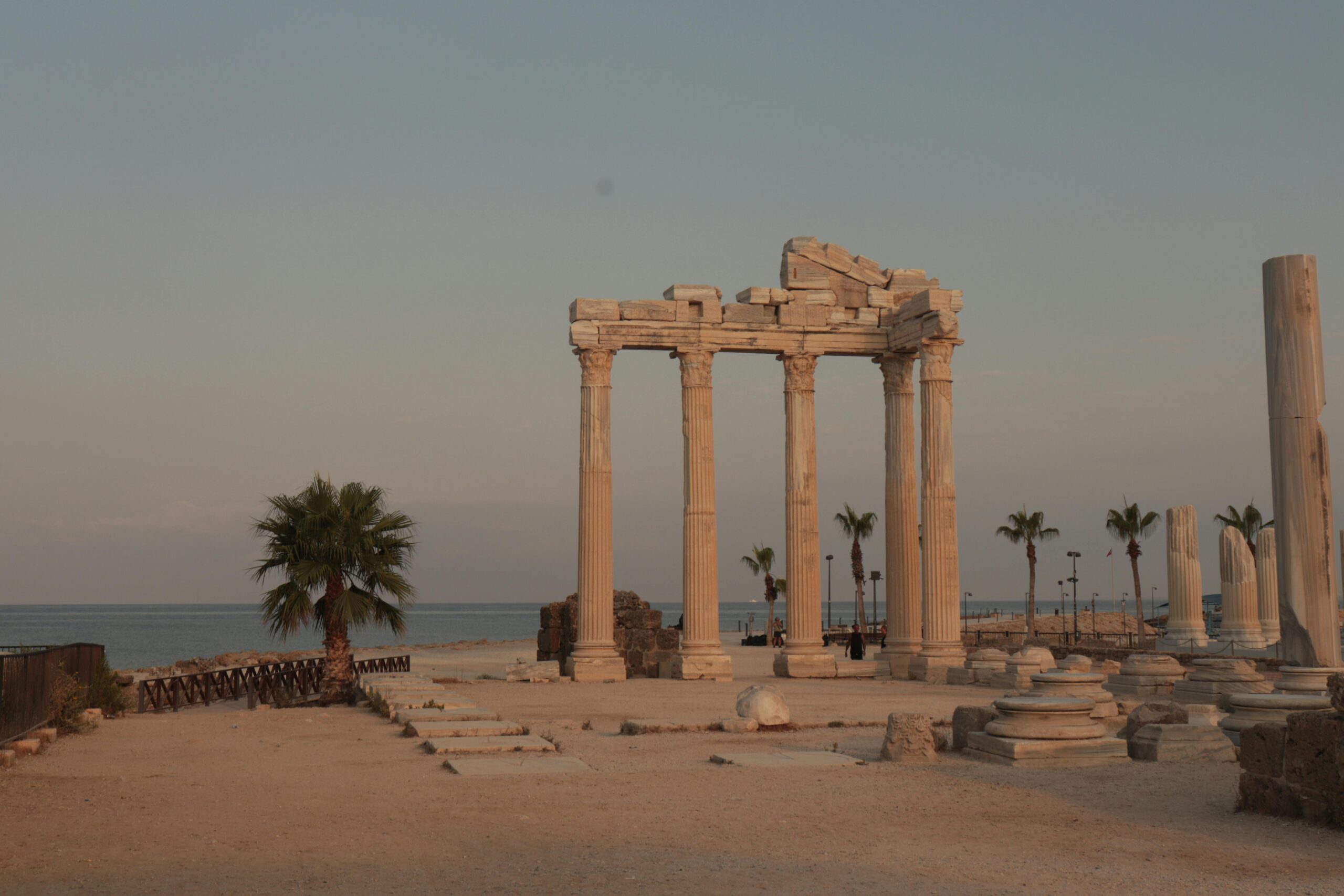 Scenic view of ancient Roman temple ruins by the sea at dusk, with palm trees.